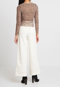 Kevyt, pitkähihaiset paita läpikuultavasta ruskeasta verkosta, jossa on hienovarainen lehmäkuvio, yhdistettynä korkeavyötäröisiin, leveisiin valkoisiin housuihin.