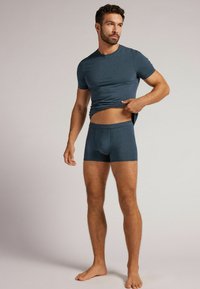 Tmavě modré přiléhavé tričko s krátkým rukávem, spárované s odpovídajícími boxerkami. Obě mají hladkou texturu a elastický pas.