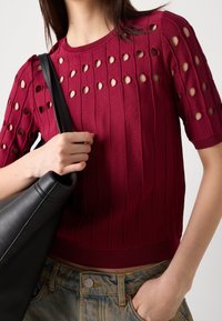 Burgundy neulepaita lyhyillä hihoilla, jossa on leikattu kuvio, ribbiteksti ja istuva helma. Yhdistettynä mustaan nahkakassiin.