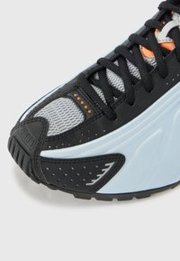 Mustat ja vaaleansiniset urheilukengät, joissa on mustat nauhat, harmaa verkko varpaiden läheisyydessä ja pieniä oransseja yksityiskohtia päälliosassa.