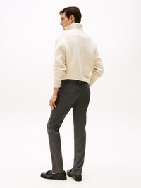 Krämfärgad stickad tröja med upphöjd geometrisk mönstring, kombinerad med grå byxor. Modellen har på sig svarta skor, med fokus på outfitens bakvy.