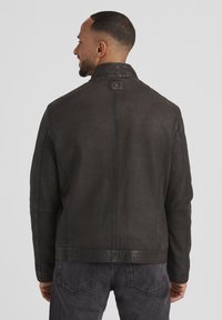 Dunkle Lederjacke mit hohem Kragen, strukturiertem Finish und sichtbaren Nähdetails. Verfügt über ein Logoschild auf der Rückseite.