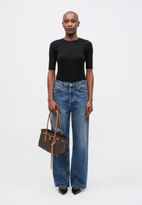 Top nero aderente, jeans larghi azzurri chiari e una borsa a tracolla marrone a fantasia con manici beige. Tacchi a punta neri completano il look.