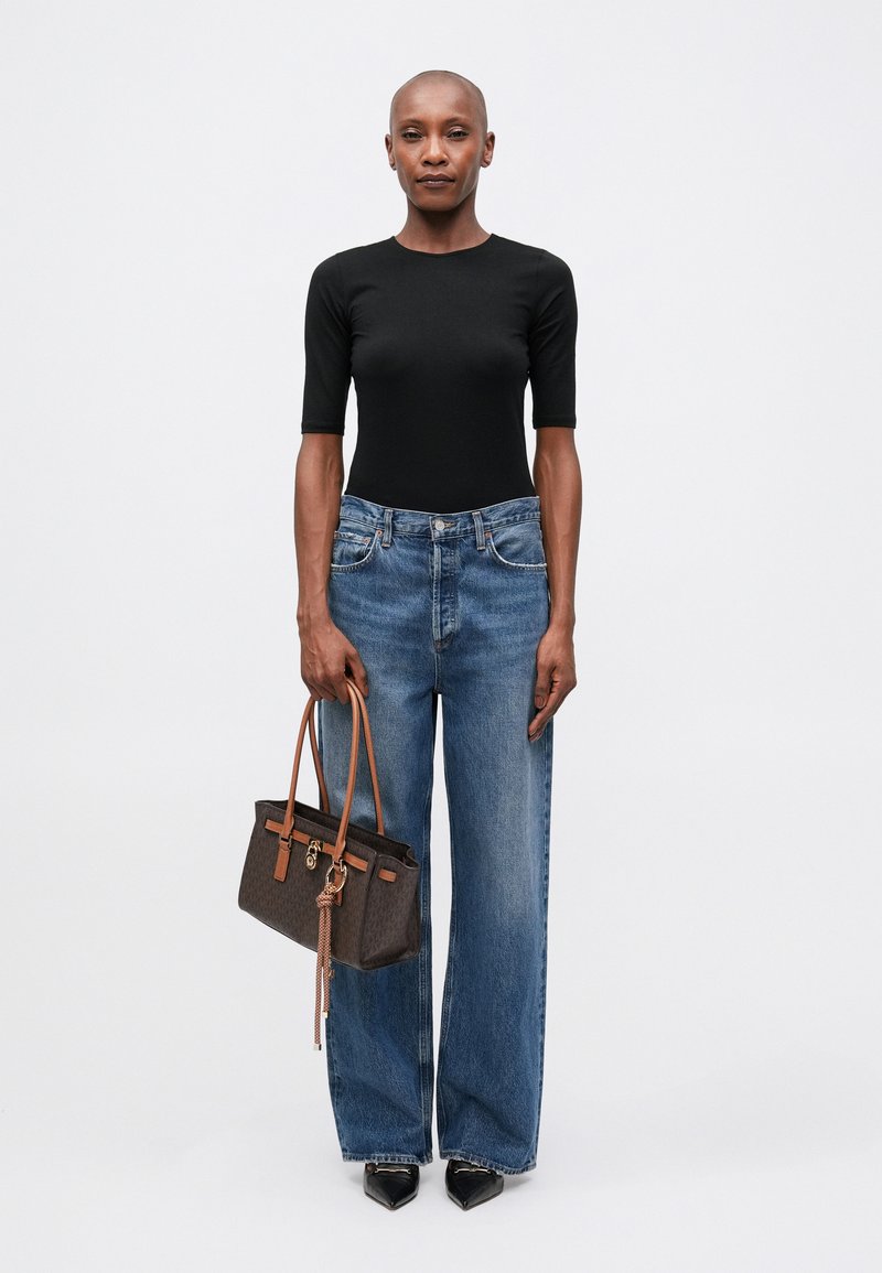 Top nero aderente, jeans larghi azzurri chiari e una borsa a tracolla marrone a fantasia con manici beige. Tacchi a punta neri completano il look.