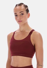 Bordó sportovní podprsenka s kulatým výstřihem, širokými ramínky a přiléhavým střihem. Vyznačuje se hladkým povrchem a diskrétním logem na spodní části.
