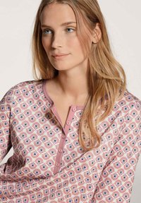 Top con motivo floreale nei colori rosa e crema. Presenta un collo rotondo, una fila di bottoni e un tessuto morbido e testurizzato.