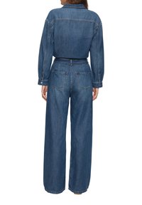 Mono de mezclilla en azul oscuro, con cuello abotonado, mangas largas, piernas anchas y dos bolsillos traseros. Tejido suave y texturizado.