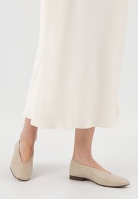 Scarpe flat beige in pelle liscia, con punta affusolata e tacco basso. Indossate con un vestito fluido di colore crema.