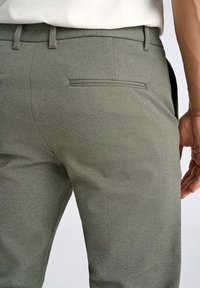Graue strukturierte Hose mit schmaler Passform, die ein dezentes Fischgrätmuster, Gürtelschlaufen und eine Rückentasche aufweist.