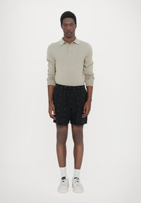 Hellgraues, gestricktes Langarm-Polo, schwarze Shorts mit kleinen weißen Mustern und weiße Sneaker mit grauen Akzenten. Einfaches Design, lässige Passform.