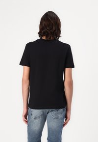 Sort bomulds t-shirt med korte ærmer, rund hals og afslappet pasform, parret med lys blå denimjeans. Ingen synlige mønstre eller detaljer.