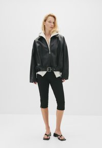 Svart läderjacka i kort modell med dragkedja fram och vit hoodie under. Kombinerad med svarta cropped byxor och svarta sandaler med remmar.