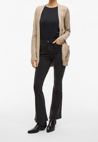 Beige cardigan, black top, and dark flared jeans. Cardigan has pockets and ribbed cuffs. Black ankle boots with buckle detail.