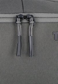 Bolsa de tela negra con cremallera y tiradores de paracord duales, con un patrón texturizado y un logotipo moldeado.