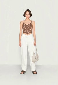 Top curto castanho com estampado floral, calças largas brancas, sandálias pretas e prateadas, e uma pequena bolsa bege com alça de corrente.