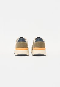 Sneaker con tomaia in suede verde oliva, dettagli in blu navy e una suola intermedia imbottita beige con un particolare arancione sul tallone.