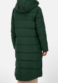 Abrigo acolchado largo de color verde oscuro con costuras horizontales, capucha y aberturas laterales. La tela parece suave y aislante para mantener el calor. Detalle negro en la capucha.