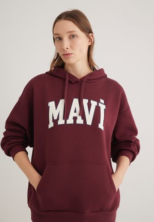 Burgundy hooded sweatshirt featuring a large white "MAVI" logo, front pocket, and ribbed cuffs. Soft texture, casual fit.
