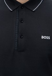 Must musta polo-särk valge kaeluse äärisega, kolm musta nööpi ja valge "BOSS" brodeeritud logoga rinnal.