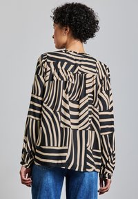 Blusa a righe nere e beige con maniche lunghe, schiena arricciata e vestibilità rilassata, realizzata in tessuto morbido con una trama liscia.