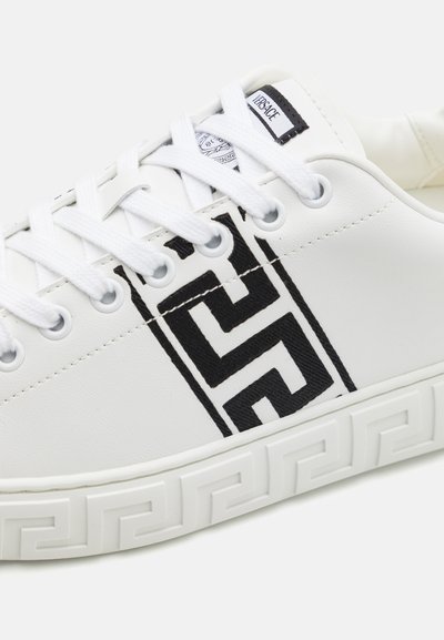 White leather sneaker with black geometric pattern, featuring white laces and a textured outsole with a Greek key design.