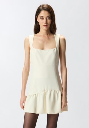Robe sans manches crème avec un décolleté carré, un corsage ajusté et un ourlet à volants évasé ; texture lisse, design minimaliste.