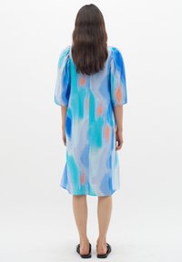 Blauwe jurk met een patroon en pofmouwen, versierd met abstracte motieven in lichtblauw, oranje en teal. Onder de knie lengte met een relaxte pasvorm.