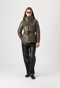 Puffer jacket in olive green, featuring a high collar, belt at the waist, and quilted texture. Paired with black leather pants and shoes.