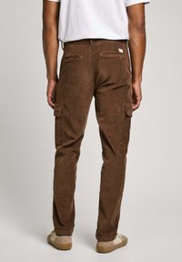 Pantalones cargo de pana marrón con corte slim, que cuentan con bolsillos laterales y un parche en la parte trasera. La textura es acanalada y la tela parece duradera.