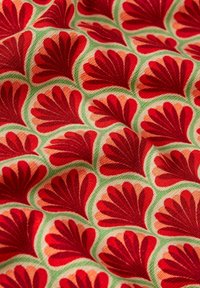 Tejido con un patrón repetitivo de formas de hojas rojas sobre un fondo beige claro, bordeado de acentos verdes. Textura suave, colores vibrantes.