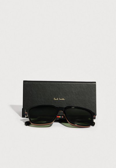 Ochelari de soare cu rame negre din acetat, lentile verzi și detalii dungate multicolore. Însoțiți de o husă de piele neagră.