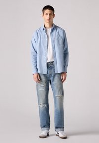 Lichtblauw gestreepte overhemd met knopen, witte t-shirt, versleten lichtblauwe spijkerbroek en zwart-witte sneakers. Eenvoudig ontwerp met zichtbare stiksels.