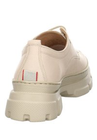 Chaussure beige à semelle épaisse avec une adhérence texturée, des coutures visibles, une languette en tissu avec des accents rouges au talon et un design à coupe basse au niveau de la cheville.