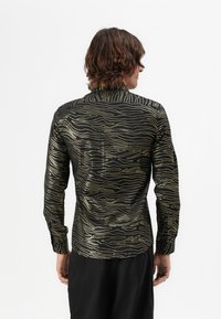 Schwarzes Hemd mit wellenförmigen goldenen Linien, langen Ärmeln und hohem Kragen. Glatte Textur, taillierte Passform und knöpfbare Manschetten. Rückansicht gezeigt.