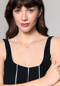 Srebrny naszyjnik w kształcie serca na kobiecie w czarnej koszulce bez rękawów w białe paski. Prosty design, gładka tekstura i minimalistyczny styl.