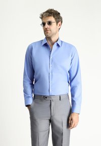 Camisa de botones azul claro con mangas largas, textura suave y botones transparentes, combinada con unos pantalones gris claro.