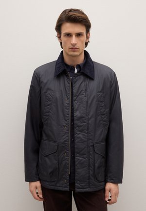 Giacca trapuntata blu navy con colletto in velluto a coste, bottoni a pressione e due tasche frontali, caratterizzata da una texture liscia e leggermente lucida.