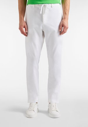 Białe bawełniane chinosy o luźnym kroju, z sznurkiem w pasie i gładką fakturą, w połączeniu z białymi trampkami.