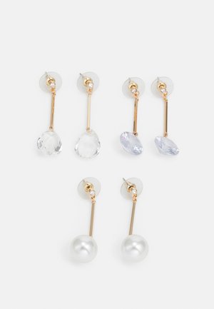 Trzy pary złoconych kolczyków wiszących z przezroczystymi i jasnopurpurowymi akcentami, z długimi prostymi paskami i okrągłymi perłowymi detalami.