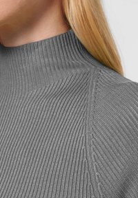 Grijze geribde coltrui met een hoge kraag, een textuurpatroon en een nauwsluitend ontwerp, met nadruk op horizontale en verticale ribbels.