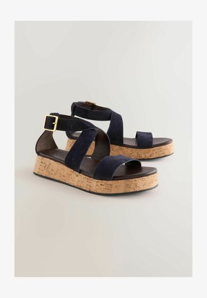 Sandales en daim bleu marine avec de larges brides, un talon plateforme en liège et un accent en boucle dorée ajustable. Design à bout ouvert.