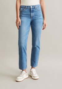 Lichtblauwe denim jeans met een hoge taille, rechte pijpen en een vijf-pocket ontwerp, gedragen met witte en beige sneakers.