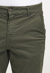 Olivgrön bomullsbyxor med en slät yta, med knäppning, bälteshällor och snedställda sidofickor.