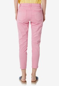 Pantalones de mezclilla rosa con pierna ajustada, bolsillos traseros y un ligero estiramiento. Presenta una cintura de altura media y dobladillos enrollados en los tobillos.