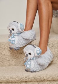 Pantofole in peluche grigio a forma di gufo con accenti blu, sciarpa a pois e suole glitterate, caratterizzate da un tessuto morbido e occhi rotondi.