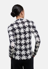 T-shirt à manches longues avec un motif géométrique noir et blanc. Fabriqué en tissu léger avec un col rond et une coupe ajustée.