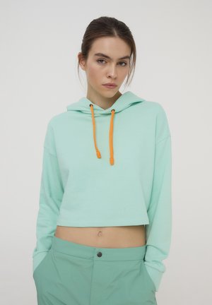 Hoodie corto verde menta con un laccio arancione. Tessuto morbido, vestibilità rilassata e maniche lunghe. Abbinato a pantaloni coordinati verde menta.