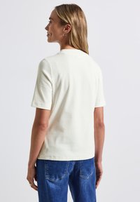 Haut à manches courtes en crème clair côtelé avec un col rond, présentant une texture subtile et une coupe décontractée, associé à un jean en denim bleu.