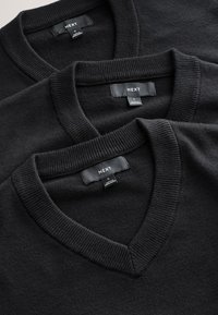 Három fekete V-nyakú pulóver, bordázott mandzsettákkal egymásra helyezve. Címkék "NEXT" felirattal és "S" mérettel. Sima textúra és egységes szín.