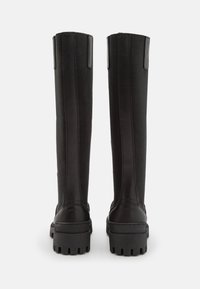Botas negras hasta la rodilla que combinan cuero liso y tela texturizada. Suela robusta con dibujo y detalles acentuados en vertical.